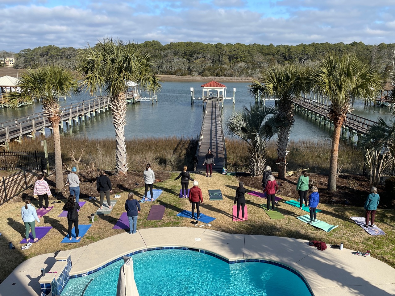 Outdoor yoga class by a pool with a scenic view of a pier and waterway, designed as part of a women's retreat to foster connection and rest.